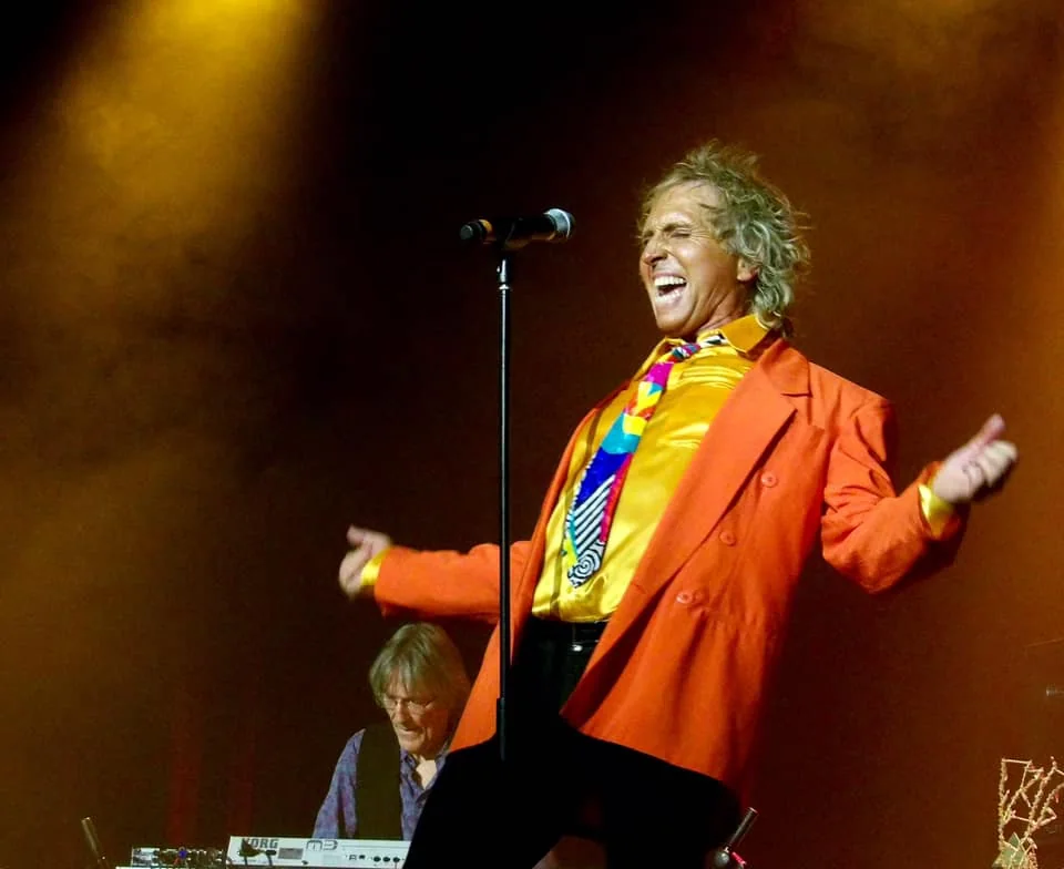 Alby Good singing in an orange jacket